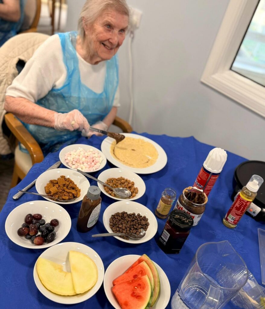 elderly woman smiles putting a variety of toppings on a pancake