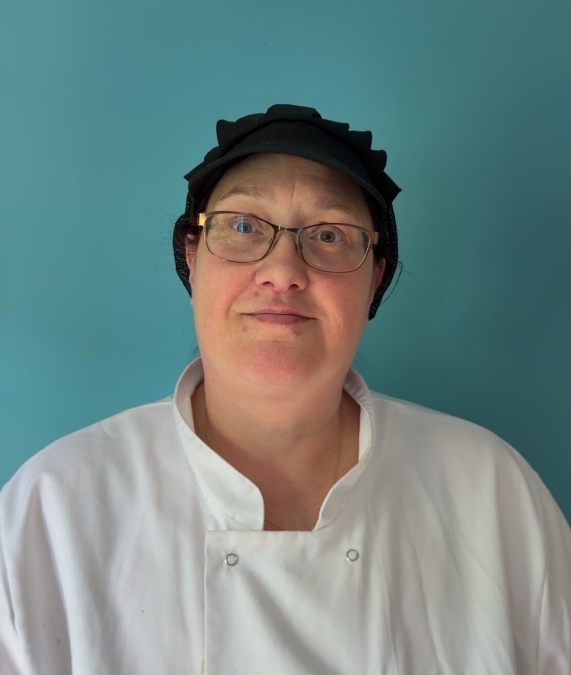 woman in chef whites and hair net smiling against turquoise background