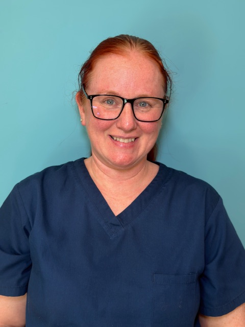 woman in dark blue nurses uniform smiling against turquoise background
