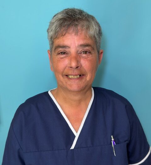 woman with short grey hair smiling in a dark blue nursing uniform