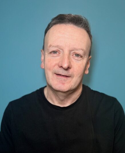 man in black t shirt in front of turquoise wall