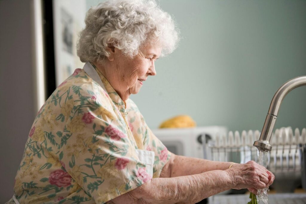 elderly woman washing her hands in a kitchen sink
